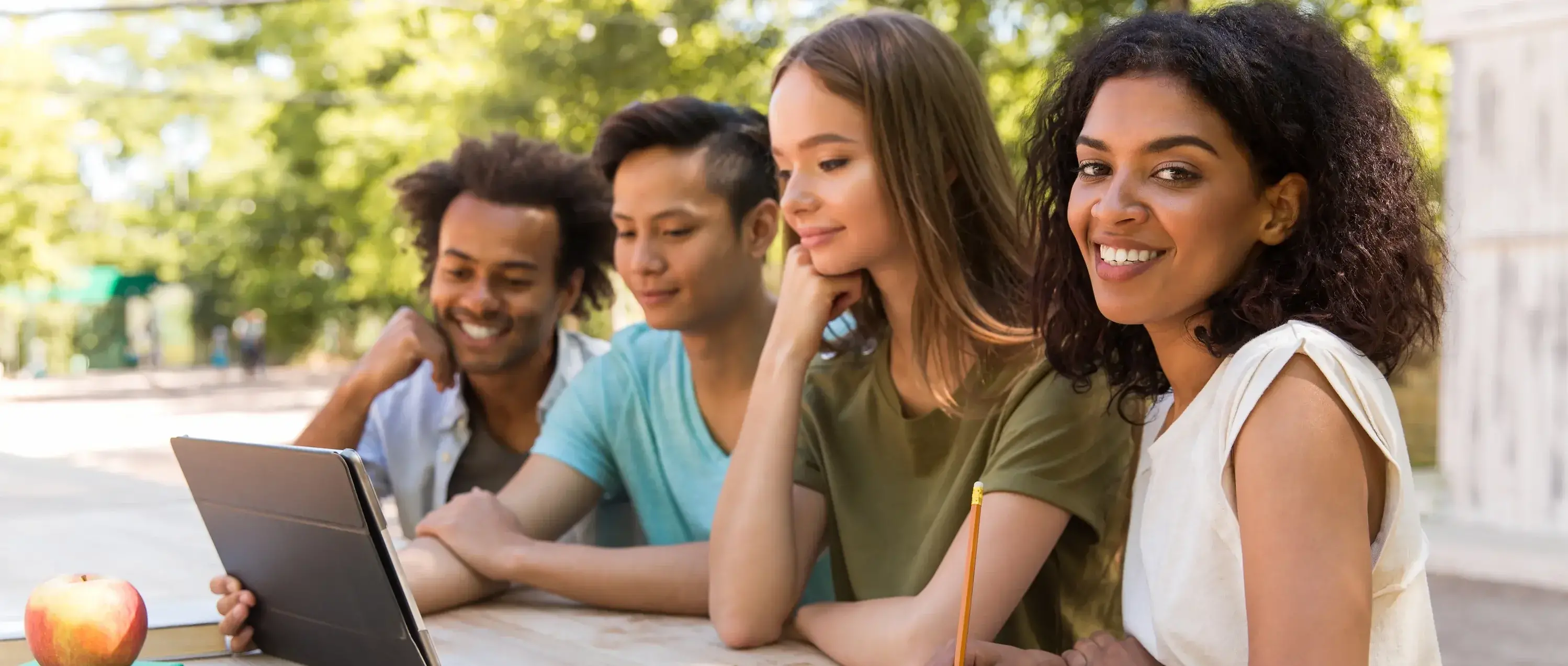 Happy young multiethnic friends students outdoors using tablet